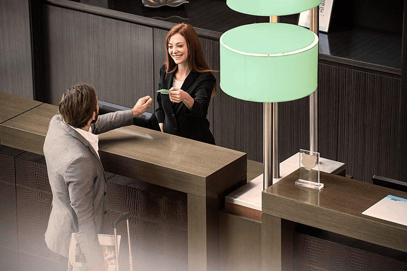 Rezeptionistin hinter einem Hotel-Tresen überreicht lächelnd eine Karte an einen Gast im Anzug