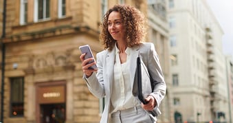 Businesswoman on the move with her laptop under her arm and smartphone in her hand, smiling