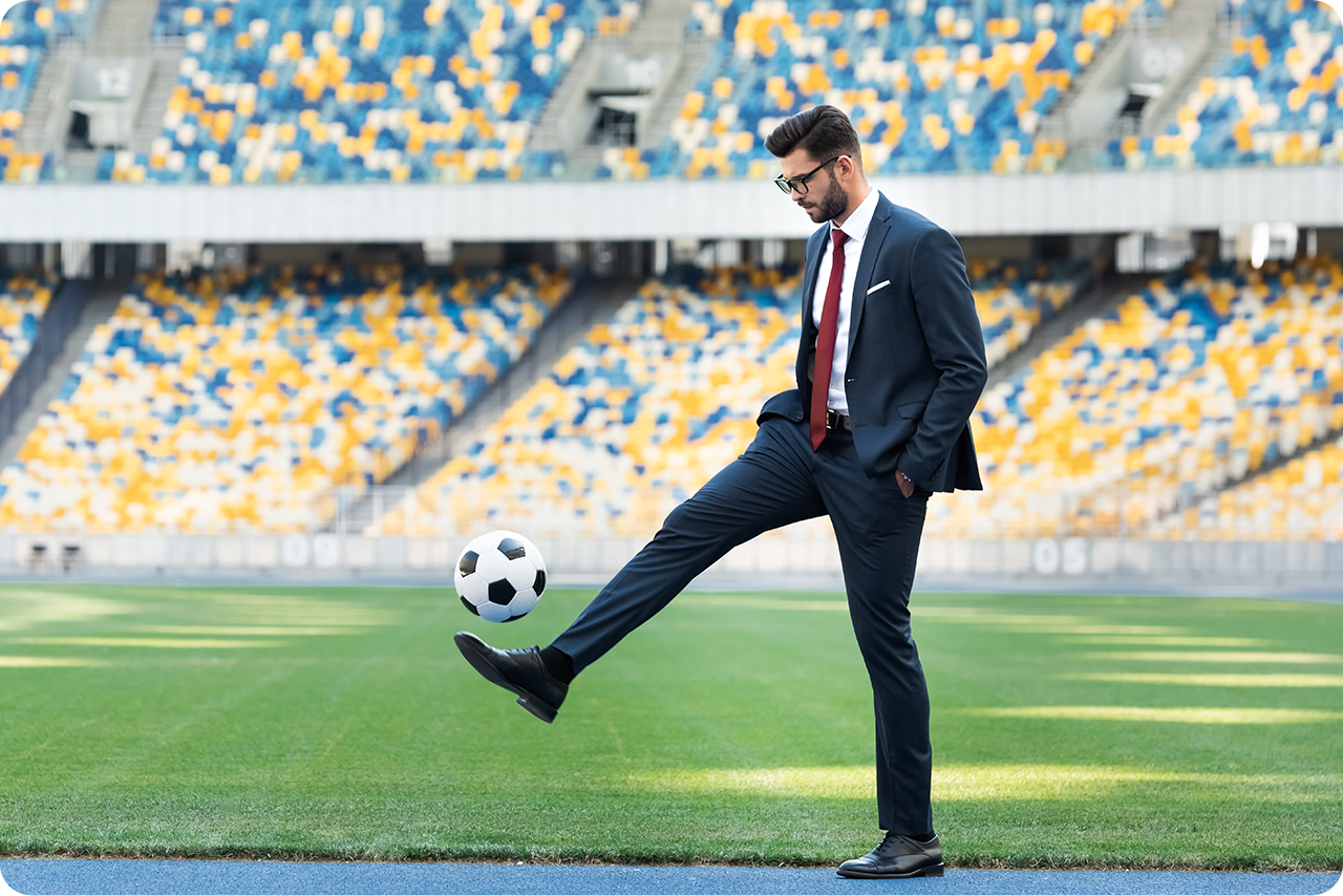 Junger Geschäftsmann in Anzug und Brille spielt mit Fußball im Stadion