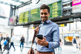 Businessman at the airport, smiling and looking down at his smartphone