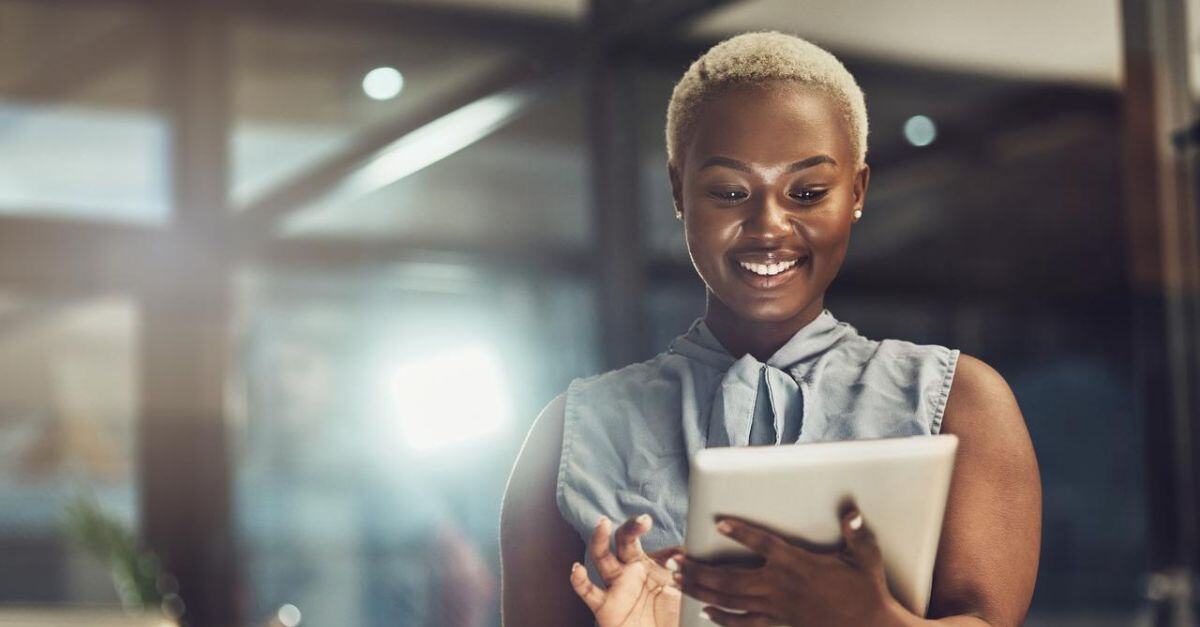 A woman smiling while working on a tablet computer in an office.